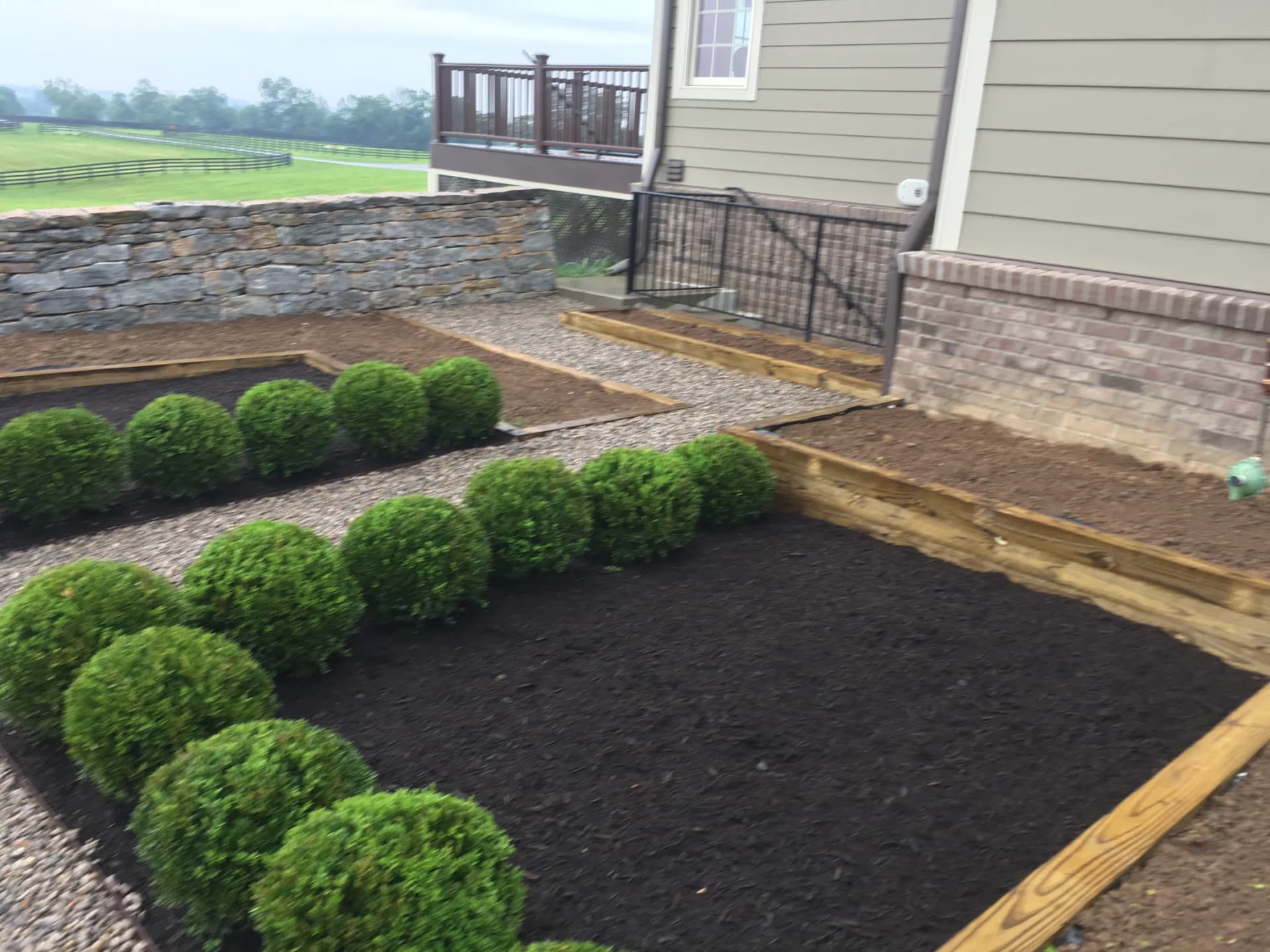 Courtyard-style garden beds with shrubs, mulch, gravel, and a stone wall in Lexington, Kentucky
