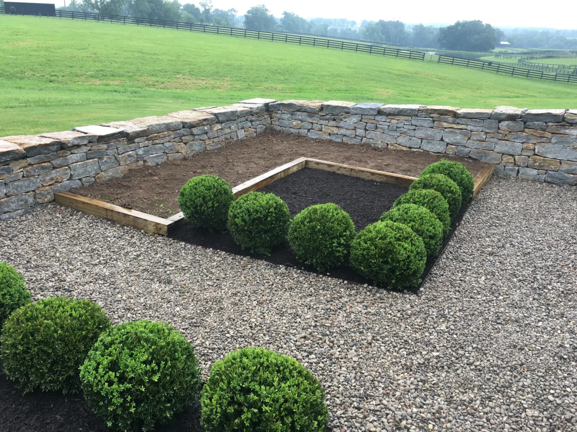 Wood-framed produce garden beds with shrub planting and gravel courtyard walkway